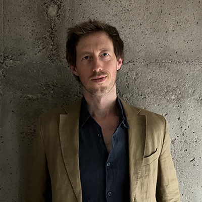 Author profile pic showing a man in a beige jacket standing against a stone wall.